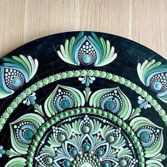 a black plate with green and blue designs on it sitting on a wooden table top