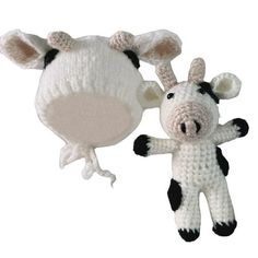 a small stuffed cow next to a crocheted hat on a white background,