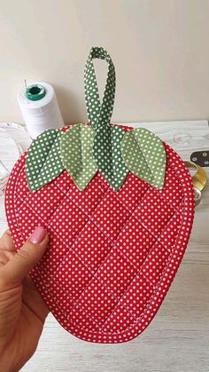 someone is holding up a piece of fabric to make a strawberry shaped pot holder with green and red polka dots on it