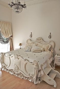 a white bed sitting in the middle of a bedroom next to a chandelier