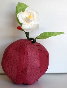 an origami apple with a white flower on top and green leaves sticking out of it