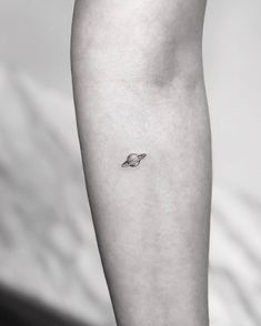 a small saturn tattoo on the left inner arm, with an arrow in the center