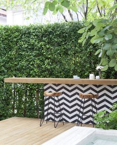 an outdoor bar with two stools in front of a green wall and wooden deck