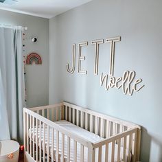 a baby's room with a white crib in the corner and a wooden name sign on the wall