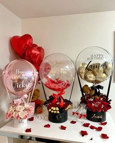 three vases filled with flowers and balloons on top of a white table next to hearts