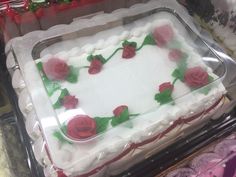 a cake with white frosting and red roses on it sitting in a plastic container