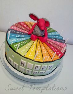 a birthday cake decorated to look like a rainbow wheel with a teddy bear on top