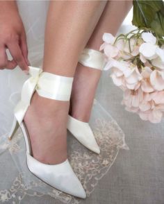 the bride is tying her wedding shoes with white satin ribbons and flowers in the background