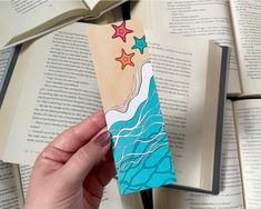 a hand holding an open book with stars on it and water in the middle, surrounded by books