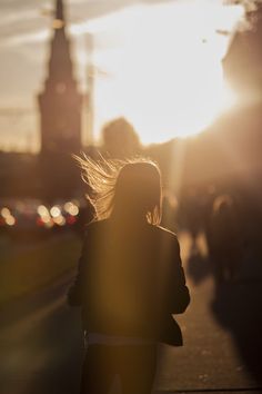 a woman is walking down the street with her hair blowing in the wind as the sun sets