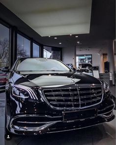 the front end of a black car in a showroom with lots of windows and doors