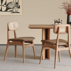 two wooden chairs sitting at a table with a vase on the wall in the background