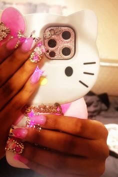 a woman's hand holding a hello kitty phone case with pink and gold decorations