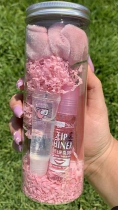 a person holding up a jar with pink stuff in it on the grass and flowers