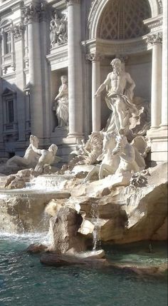 a fountain in front of a building with statues on the sides and water flowing from it