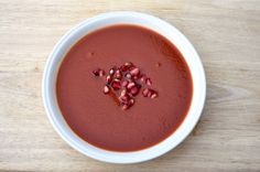 a white bowl filled with red soup on top of a wooden table and garnished with pomegranates