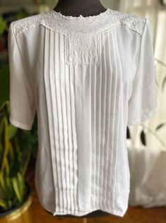 "Vintage 90s white blouse with a floral collar by Nicola. Pleated in the front and buttons at the back of the neck. 100% polyester. Condition: Great. No holes. Has two super faint stains. See photos. Size: tagged 10. Best fit M. Always refer to measurements for more accurate sizing. Measurements taken laying flat: STS: 16\" PTP: 19\" L: 25\" ALL SALES ARE FINAL SO PLEASE DOUBLE CHECK THE MEASUREMENTS PRIOR TO BUYING AND DON'T HESITATE TO REACH OUT IF YOU HAVE ANY QUESTIONS!  All items are vintage/preloved and may have small imperfections. This should be expected for secondhand clothing. ALL MAJOR FLAWS WILL BE NOTED IN THE DESCRIPTION AND PHOTOGRAPHED." White Tops With Lace Trim And Peter Pan Collar, White Spring Shirt With Lace Collar, White Shirt With Lace Collar For Spring, Classic White Tops With Peter Pan Collar, Classic White Top With Peter Pan Collar, Formal Summer Tops With Lace Collar, White Lace Top For Formal Occasions, Formal White Lace Top, Classic Summer Tops With Lace Trim