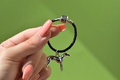 a woman holding a black bracelet with two small silver horses on it's side