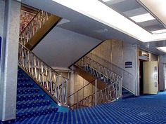 an empty hallway with blue carpeting and metal handrails on the wall, next to a set of stairs