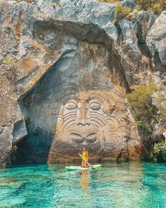 a person in a kayak paddles past a carved face on the side of a cliff