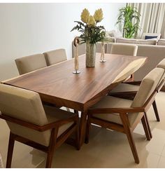 a wooden table surrounded by beige chairs and vase with flowers on it in a living room