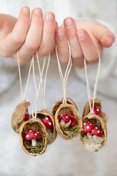 three small mushrooms are hanging from twine with moss and little red mushrooms in them