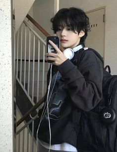 a person with headphones on taking a selfie in front of some stairs holding a cell phone