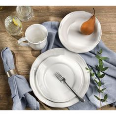 the table is set with plates, silverware and a pear on top of it