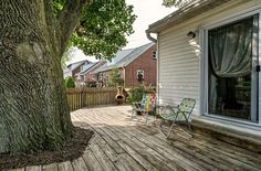 a wooden deck with two chairs next to a large tree in front of a house