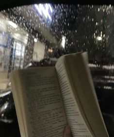 an open book sitting on top of a table in front of a window covered in rain