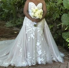 a woman in a wedding dress standing next to some bushes and trees with flowers on it