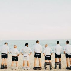 a group of men standing next to each other on top of a sandy beach near the ocean