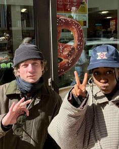 two people standing in front of a doughnut shop making the peace sign with their hands