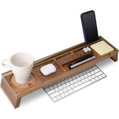 a wooden desk with a keyboard, mouse and coffee cup on it next to a cell phone