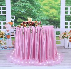 a pink table cloth with flowers and candles on it in front of an open window