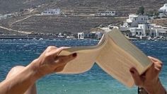 a person is reading a book by the water's edge while holding it up to their face