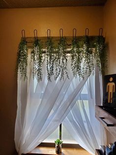 an open window with white curtains and plants hanging from it's rodulage