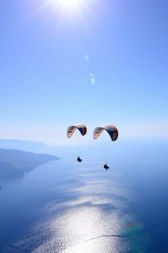 two parasailers are flying over the ocean under a bright blue sky and sun