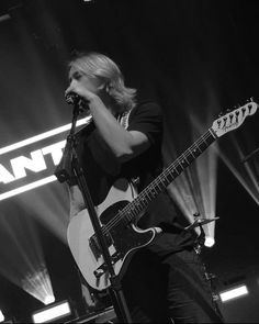 a woman singing into a microphone while holding a guitar in front of her and playing the guitar