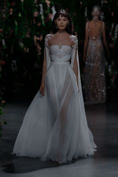 a woman in a white gown and veil walking down the runway at a fashion show