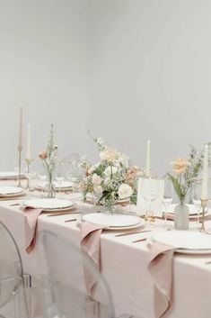 the table is set with white plates and pink napkins, flowers in vases, and candles