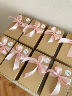 six boxes with pink bows and name tags on them, all wrapped in brown paper