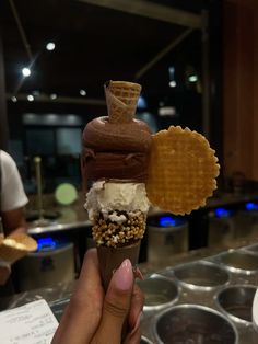 a person holding up an ice cream cone with chocolate and nuts on it, in front of other food items