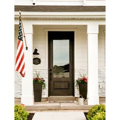 an american flag hangs on the front door of a white house with potted plants