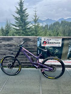 a purple mountain bike parked in front of a wooden fence with mountains in the background