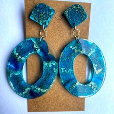 a pair of blue and green earrings sitting on top of a piece of brown paper