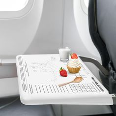 an airplane tray with a cupcake and strawberries on it next to a glass of milk