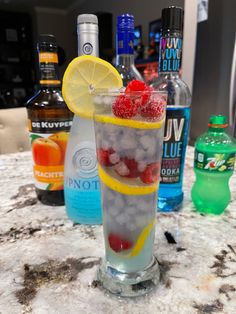 a tall glass filled with ice and fruit on top of a counter next to bottles