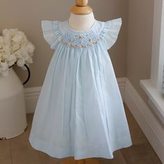 This Baby Girl's Blue Smocked Dress Is Too Cute!! The Dress Is Done In A Pale Blue Voile Atop A White Liner (Poly/Cotton Blend For Easy Care). The Semi-Sheer Voile Adds A Wispy, Dressy Look (True To Many Of Luli & Me's Designs) The Smocked Neckline Has Gorgeous Hand-Embroidered Flowers Done In Shades Of Pink With Light Green, Blue And Yellow Accents, All Atop An Embroidered Lattice Design. The Shoulders Have A Double Ruffle Flutter Sleeve, Which Add Even More Sweetness To The Dress. A Matching B Cute Blue Dresses With Smocked Cuffs, Cute Blue Dress With Smocked Cuffs, Cute Light Blue Dress With Smocked Back, Blue Smocked Dress With Flutter Sleeves And Ruffles, Cute Blue Smocked Dress With Ruffles, Light Blue Smocked Dress With Ruffled Short Sleeves, Blue Dress With Smocked Bodice For Playtime, Blue Smocked Dress With Cuffs For Playtime, Cotton Smocked Dress With Ruffles For Baptism