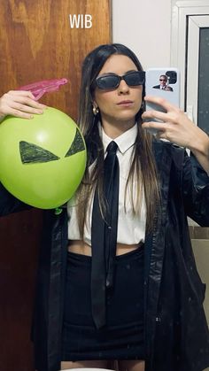 a woman wearing sunglasses holding a balloon and taking a selfie with her cell phone